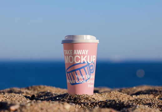 A takeaway cup mockup sits on sandy beach,