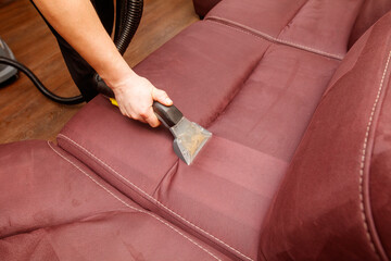 A person is cleaning a couch with a vacuum cleaner