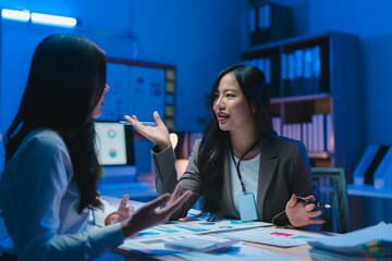 Two businesswomen discussing over financial reports in office meeting room at night