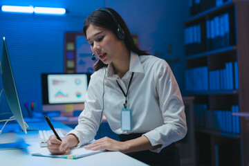 Focused employee working overtime at her desk in a modern office with blue light
