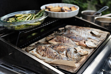 Grilled fish on a grill as a meditteranean meal ready to eat. Dorada fish on a board made during barbecue outdoors. Delicious and healthy food for lunch or main dinner. Close up.
