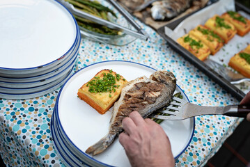 Grilled fish with gratin and chives on plate. Preparation food on a table for lunch or dinner on barbeque. Healthy mediterranean meal during garden party or in restaurant. Dorada fish ready to eat.