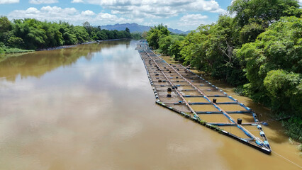 Red tilapia cages in the Mae Klong River, with Thai workers feeding and watching the floating tilapia being raised in used plastic containers in the Mae Klong River in Thailand