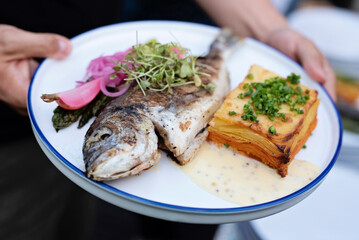 Grilled fish on a plate as a main dinner or lunch ready to eat. Plate on hands of chef with healthy food and dorada fish. Fresh meal in restaurant. Close up.