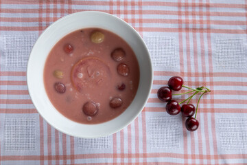 chilled cherry soup with fresh cherries on checkered tablecloth top view