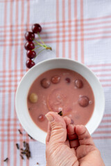 hand holding a clove above cherry soup with fresh cherries on checkered tablecloth
