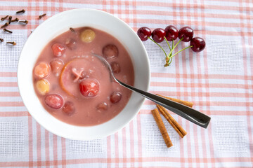 Cherry soup with whole fruits, spices and spoon top view

