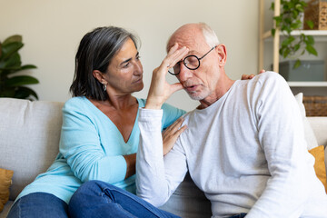 Mature woman consoling depressed husband sitting on the sofa at home living room.