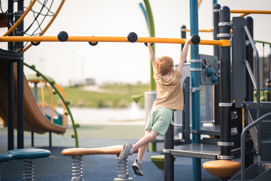 Young boy builds strength swinging on colorful monkey bar set