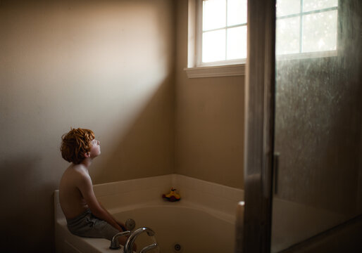 Soft light falls on boy during quiet indoor bath scene