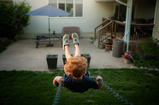Young boy swinging high in backyard on summer evening