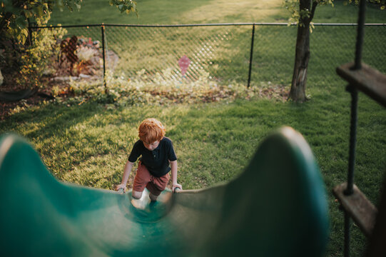Redhead boy climbs slide alone in backyard summer light