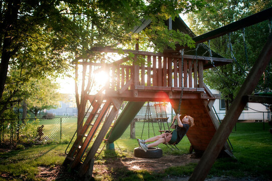 Young boy swinging under treehouse during golden summer light