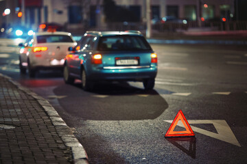 Reflective red warning triangle placed on dark road at night after rear-end collision between two vehicles to alert traffic and ensure safety in emergency conditions. Traffic hazard scene at night