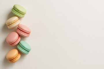 Obraz premium Pastel macaron assortment on textured white background with soft natural light creating delicate and inviting atmosphere for sweet dessert lovers