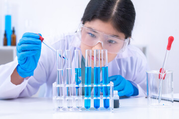 Teen scientist girl conducting science test by carefully evaluating blue solution in laboratory....