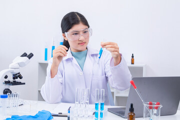 Teen girl scientist in labcoat and safety glasses performing chemistry experiment with pipette and...