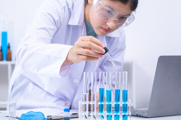 Teen scientist girl conducting science test by carefully evaluating blue solution in laboratory....