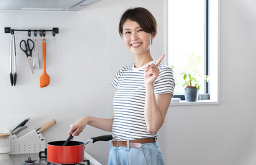 キッチンで料理をしながら指差しをする女性