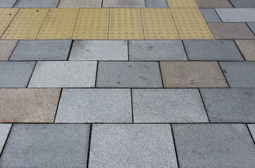 Gray and brown pavement with yellow tactile tiles for blind handicap. Yellow tactile paving on...
