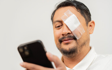 Close-up shot of delighted adult man with eye patch over white background and using mobile phone...