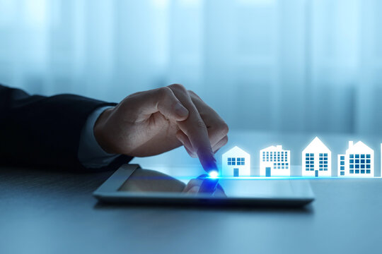 Real estate agent looking for housing via tablet at table, closeup. Different buildings icons on device screen - Powered by Adobe