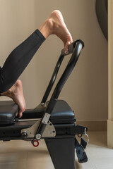 Close up detail of a pilates reformer machine with springs, carriage, and a person exercising