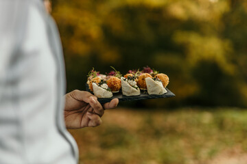 Waiter holding slate plate with gourmet appetizers at outdoor event