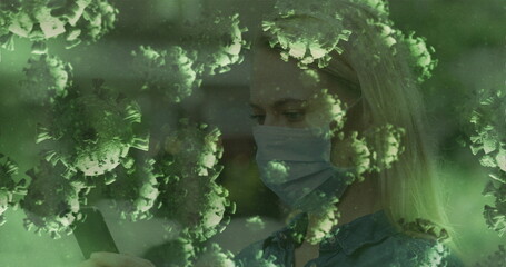 Checking smartphone woman wearing medical mask and denim shirt in dimly lit room, virus particles