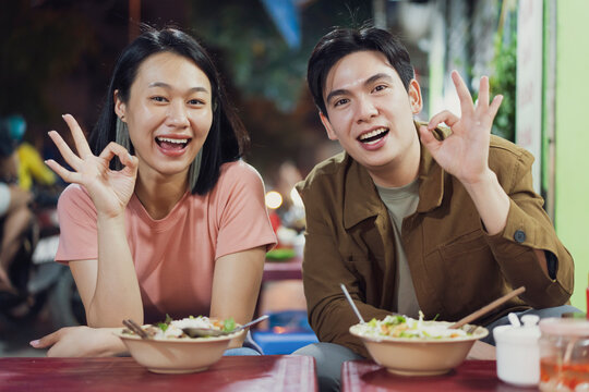 Young couple enjoying dinner at a bustling Hanoi street food stall during the evening