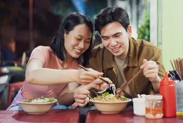 Couple enjoying traditional Vietnamese cuisine at a bustling Hanoi street food stall during the...