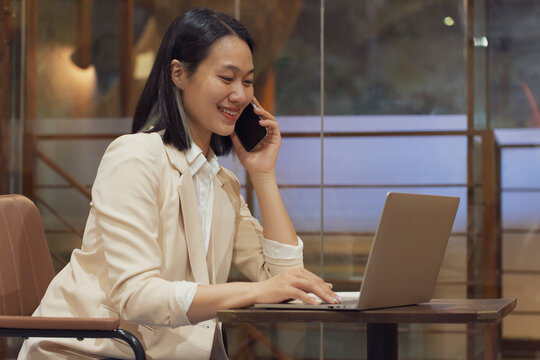 Businesswoman using laptop and phone in modern cafe in Hanoi, Vietnam during afternoon work hours
