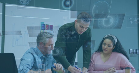 Reviewing professionals writing notes on papers in meeting room, with laptop and digital overlays