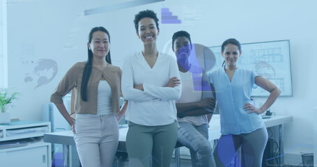 Standing four professional women in business casual wear posing in office, with desks and monitors