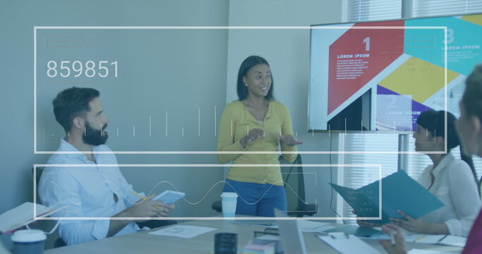 Presenting businesswoman gesturing toward charts on screen at conference room, with laptops