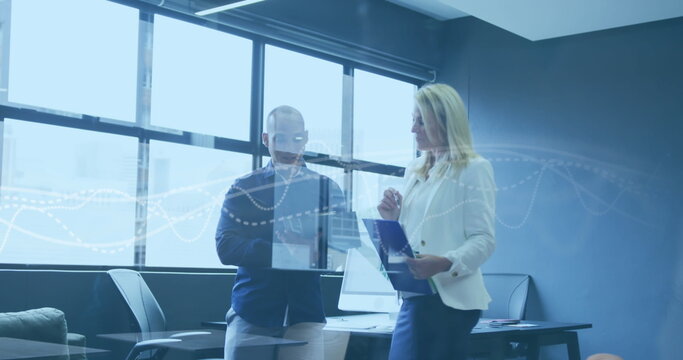 Standing colleagues holding clipboard and tablet in office near window, digital chart overlay