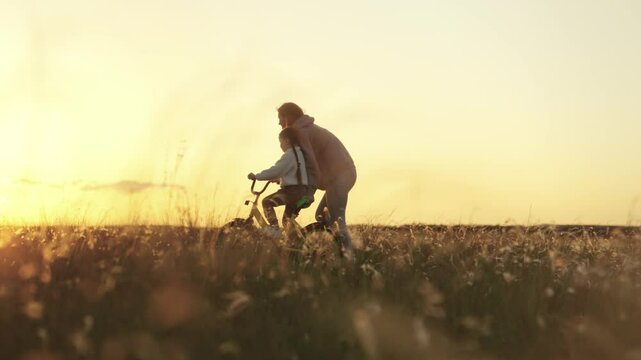 Mother Teaching Child To Ride A Bike At Sunset, Happy dad and daughter, Countryside joy, Summer bike ride, Innocent childhood, True family values, Enjoying nature together, Father helping child