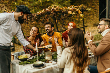 Friends clapping as chef serves dessert at an outdoor autumn dinner party