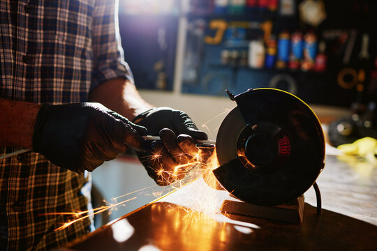 Metalworker sharpening metal rod with bench grinder creating sparks in workshop