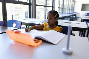 Orange pencil case lying open on desk with notebook and gray stand in classroom, copy space