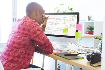 Designer studying vehicle blueprints on monitor with graphic tablet and potted plant in workspace