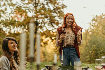 Woman holding wine glass, toasting friends at outdoor autumnal party