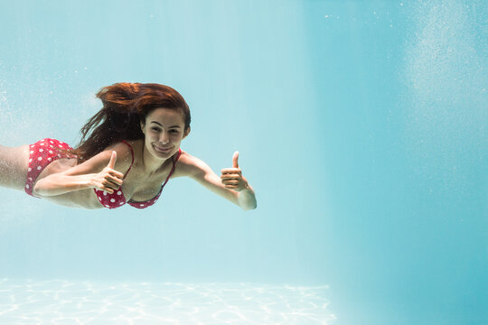 Fototapeta Swimmer wearing red polka dot bikini is floating in clear pool water and giving thumbs-up