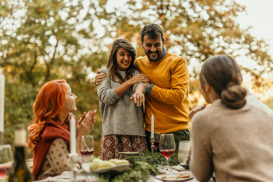 Happy couple showing engagement ring to friends at outdoor party