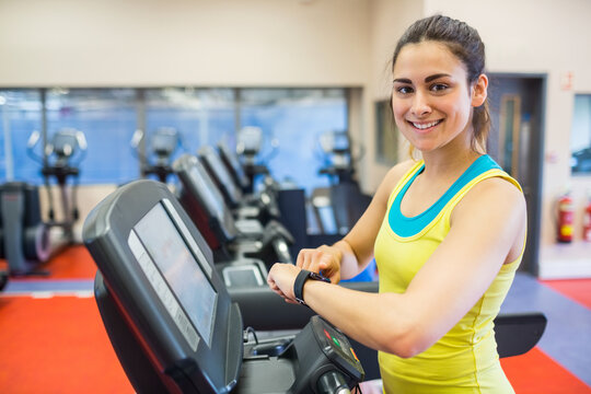 Fototapeta Hispanic woman standing on treadmill console wearing smartwatch in gym by windows, cardio machines