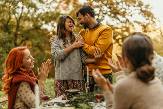 Happy couple embracing while friends applauding at outdoor celebration dinner