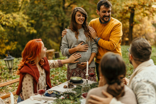 Happy pregnant woman sharing news with friends at outdoor autumn party