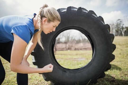 Fototapeta Large tractor tire resting on grassy field under cloudy sky, with bare trees in distance