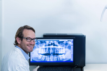 Computer workstation displaying panoramic dental X-ray in exam room, with lamp arm and keyboard