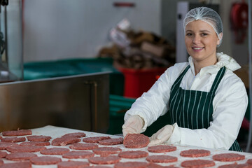 Woman organizing raw hamburger patties on table at meat plant wearing protective gear, copy space
